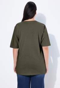 Olivegrünes, übergroßes T-Shirt mit kurzen Ärmeln, Rundhalsausschnitt und weicher Textur, kombiniert mit blauen Jeans. Rückansicht gezeigt.