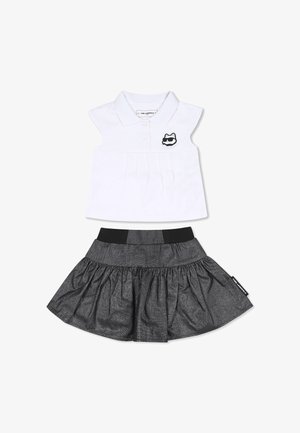 Ensemble deux pièces comprenant une chemise polo blanche avec un devant plissé et un logo de chat noir, assortie d'une jupe noire évasée avec une taille élastique.