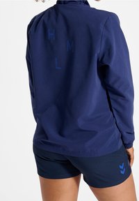 Marinblå vindjacka med framfickor, prydd med blå tryckta bokstäver "H", "M", "L" på ryggen; matchas med matchande shorts.