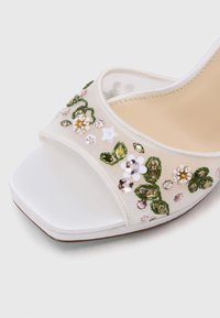 Sandal aperto bianco con punta quadrata, decorato con fiori in paillettes e perline verdi, rosa e bianche; texture liscia simile alla seta.