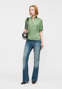 Πράσινη σατέν μπλούζα με κουμπιά μπροστά και κοντά μανίκια, σε συνδυασμό με φαρδιά ξεβαμμένα μπλε τζιν. Αξεσουάρ περιλαμβάνει μια μικρή μαύρη τσάντα.