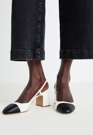 Piedi che indossano scarpe slingback bicolore nero e bianco con tacco a blocco abbinate a pantaloni cropped di denim nero.