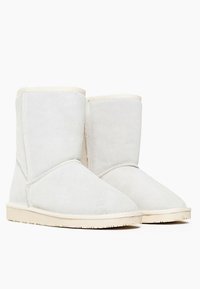 Botas de ante blancas hasta el tobillo con punta redondeada, detalles de costura y una suela de goma beige. Es probable que el interior esté forrado para mayor calidez.