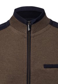 Braune strukturierte Jacke mit hohem Kragen, Reißverschluss und marineblauen Akzenten an Schultern und Tasche. Verfügt über ein meshartiges Textildesign.