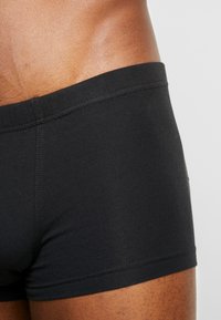 Black cotton boxer briefs feature a smooth texture, a soft waistband, and a fitted design, highlighting the contours of the wearer’s waist.