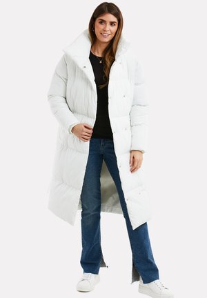 Hvid pufferjakke med høj krave, knapdetaljer og en lang, lige pasform. Sammen med mørke jeans og hvide sneakers.