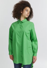 Green, long-sleeve shirt made of smooth, lightweight fabric with a button-down front and a slightly curved hemline.