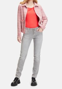 Rosa tweedjacka, orange topp, ljusgrå jeans och svarta snörskor. Jackan har krage och framfickor, jeansen har slim fit.