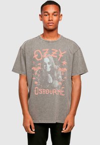 Tricou supradimensionat gri, din bumbac, având un grafic estompat cu o figură cu păr lung, palmieri și numele "Ozzy Osbourne" în text roz.