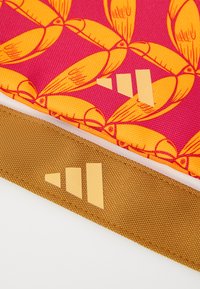 Material colorat cu un fundal roz și modele de pești galbeni, combinat cu o curea texturată maro care prezintă accente geometrice portocalii.