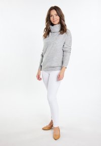 Lichtgrijze gebreide coltrui, lange mouwen, gecombineerd met witte slim fit jeans en tan puntige hakken. Minimalistisch ontwerp met een zachte textuur.