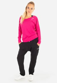 Pantaloni jogger neri larghi con tasche laterali e una maglietta a maniche lunghe rosa. La maglietta ha un collo largo e un piccolo logo sul petto.