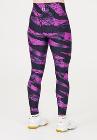 Person som bär svarta och lila mönstrade leggings och vita FZ Forza-sneakers sett bakifrån mot en vit bakgrund.