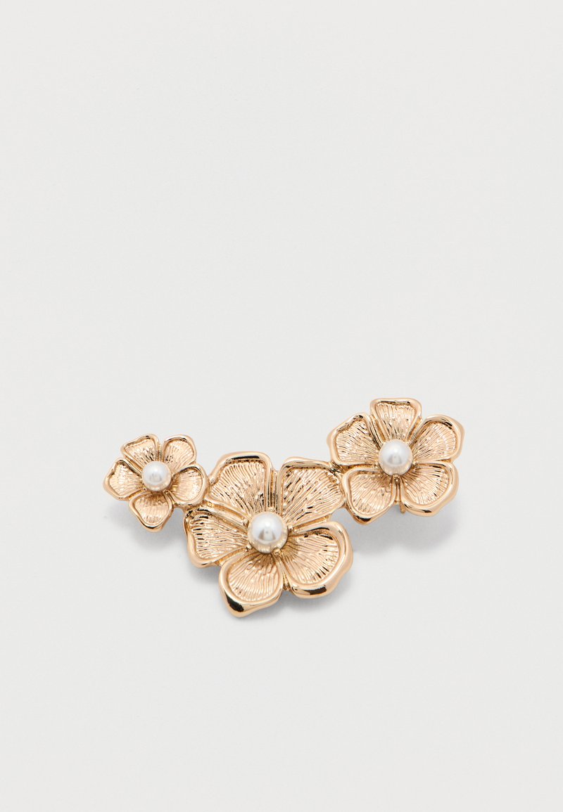 Τρεις χρυσές καρφίτσες σε σχήμα λουλουδιού με υφή στα πέταλα, καθεμία με ένα κεντρικό λευκό μαργαριτάρι, τοποθετημένες σε απλό λευκό φόντο.