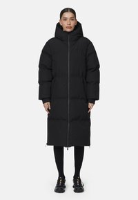 Lungo cappotto imbottito nero con colletto alto e cappuccio, dotato di chiusura frontale con zip e sezioni trapuntate per l'isolamento.