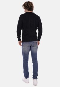Maglione nero a maglia con pattern a diamante tessurizzati, polsini e orlo a costine, abbinato a jeans blu e scarpe bianche, visto da dietro.