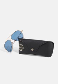 Ochelari de soare Ray-Ban cu lentile albastre, rame din metal aurit și un toc moale negru cu logo și închidere tip snap.