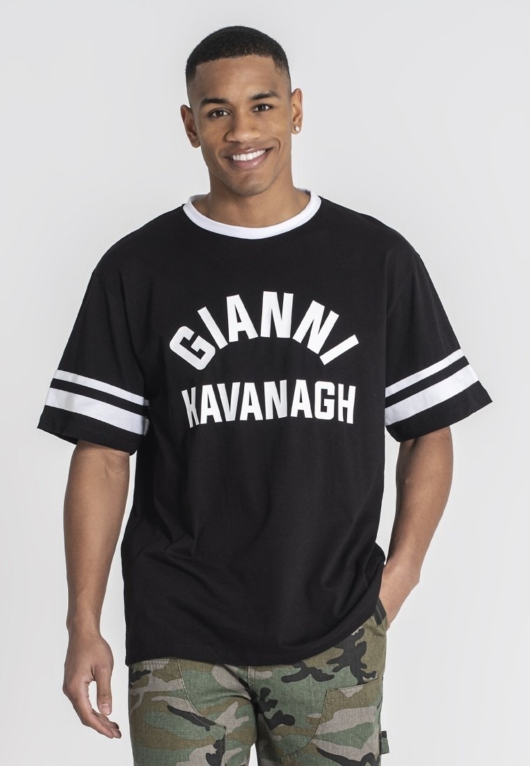 Čierne oversized tričko s bielym textom "GIANNI KAVANAGH" a bielymi pruhmi na rukávoch. Spárované s nohavicami v maskáčovom vzore.