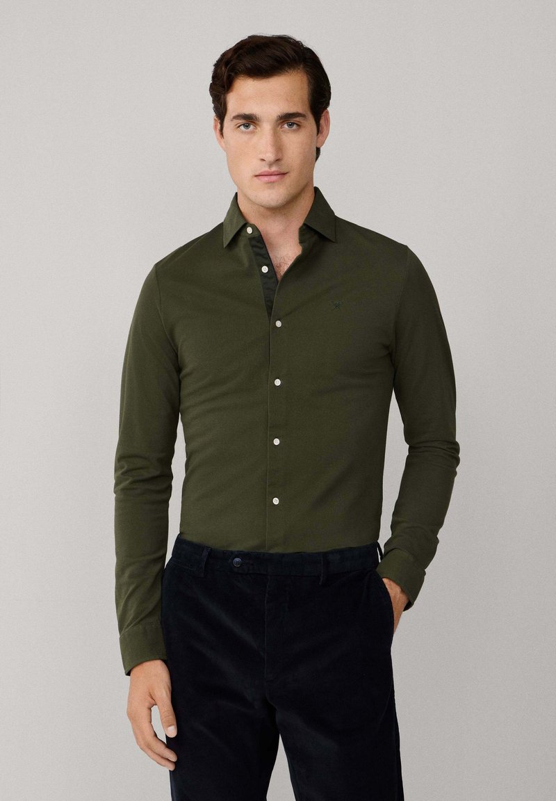 Olijfgroene button-up overhemd met een spitse kraag, lange mouwen en witte knopen. Draagt met zwarte corduroy broek. Gestructureerde stof.