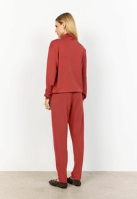 Roestkleurige loungewear set met een coltrui en bijpassende broek. Zachte stof, comfortabele pasvorm en taps toelopend ontwerp.