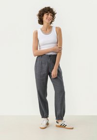 Top bianco a canotta abbinato a pantaloni larghi in lino grigio con polsini elasticizzati e tasche anteriori, indossato con sneakers bianche e lacci a motivo.