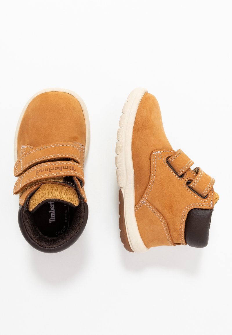 Bottes enfant en suède beige avec semelles blanches, doubles bandes Velcro et col des chevilles rembourré marron foncé, vues de dessus et de côté.