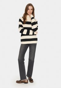Schwarz-creamfarben gestreifter Rollkragenpullover, kombiniert mit dunkelgrauen Jeans und braunen Slippern. Der Pullover hat eine lockere Passform und eine weiche Textur.
