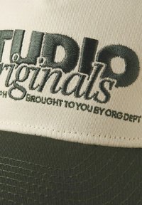 Beige caps med grøn skygge, med broderet sort tekst "STUDIO Originals" og "BROUGHT TO YOU BY ORG DEPT" i et stilfuldt skrifttype.
