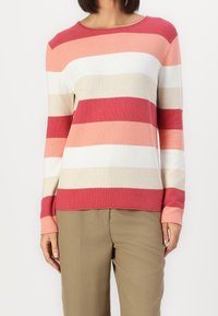 Pull rayé rouge et rose avec manches longues, encolure ronde et texture douce, associé à un pantalon beige.
