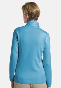 Pull-over à manches longues bleu clair avec un col montant, fabriqué en tissu lisse et texturé avec un motif subtil. La vue de dos montre une coupe ajustée.