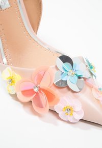Chaussure à talon haut beige à bout pointu, ornée de fleurs en plastique multicolores et de strass, avec une finition en cuir lisse.