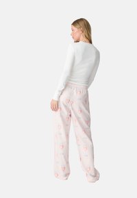 Maglietta bianca a maniche lunghe abbinata a pantaloni da pigiama rosa pastello con un motivo di bicchieri e piattini, cintura elastica e vestibilità comoda.