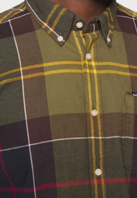 Košile s knoflíčky v kostkovaném vzoru se zelenou, žlutou, burgundskou a krémovou barvou. Obsahuje límec, zapínání na knoflíky a náprsní kapsu.