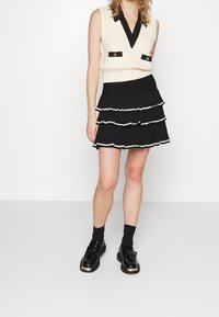 Krémová bezramenná top s pleteným vzorem a černým límečkem a knoflíky, spárovaná s černou vrstvenou sukní s bílým lemem. Černé mokasíny a ponožky.