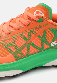 Orangene Sportschuhe mit grünen Akzenten und detaillierter Mesh-Überlagerung, ausgestattet mit einer strukturierten Sohle und einem gemusterten Design im oberen Bereich.