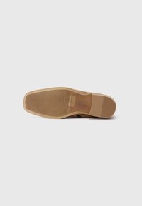 Zool van een bruine leren nette schoen met een vierkante neus en een gestructureerde rubberen grip, weergegeven tegen een effen witte achtergrond.