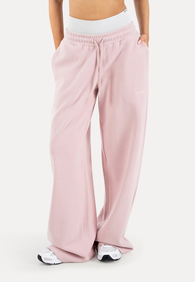 Pantalon de survêtement ample rose clair avec taille à cordon, porté avec des baskets blanches et un haut court blanc.