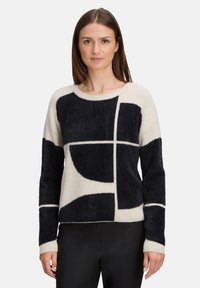 Zwarte en crèmekleurige gebreide trui met geometrische vormen, textuurstof, ronde halslijn en lange mouwen, gecombineerd met zwarte broek.