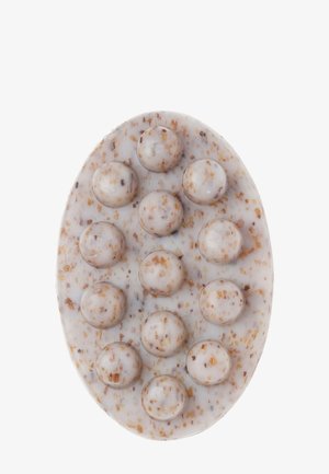 Savon naturel ovale avec des perles exfoliantes rondes intégrées et des taches brunes visibles sur fond blanc.