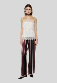 Camisola bianca con bordo di pizzo abbinata a pantaloni larghi a righe bordeaux e blu navy. Texture liscia e dettaglio in vita arricciato.