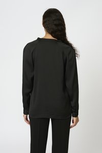 Maglietta nera a maniche lunghe con tessuto testurizzato, scollatura rotonda e spalle leggermente arricciate. Abbinata a pantaloni neri, vista da dietro.