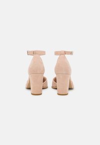 Nude suede high-heeled sandals with ankle straps and block heels, featuring a smooth texture and a subtle sheen on the sole.