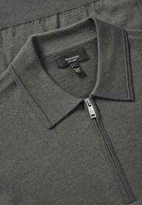 Polo in lana merino verde con zip, colletto piatto e texture a coste. Etichetta che recita “Matinique”, taglia L.