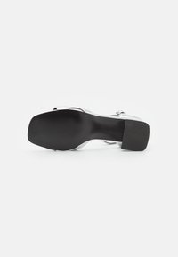 Silver högklackad sandal med en svart gummisula, med en slät metallisk yta och design med ankelrem. Texturerad botten för bra grepp.