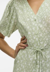 Robe florale verte avec des manches courtes bouffantes, décolleté en V, boutons à l'avant et une ceinture assortie à la taille, fabriquée en tissu léger.