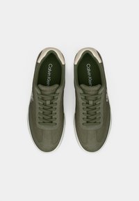 Ζευγάρι ελιάς πράσινα παπούτσια Calvin Klein με κορδόνια και λευκές λεπτομέρειες, σε θέαση από πάνω σε λευκό φόντο.