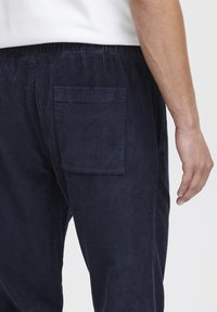 Navy corduroy pants with vertical ribbed texture, elastic waistband, and a single back pocket. Partially visible side of a hand.