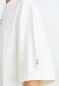 Fehér, oversized pamut póló, sima textúrával. Arany Jumpman logóval a bal ujján. Egyszerű dizájn.