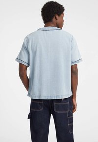 Lichtblauw denim overhemd met korte mouwen en een afgesneden kraag, met een ontspannen pasvorm en contrasterend stiksel.