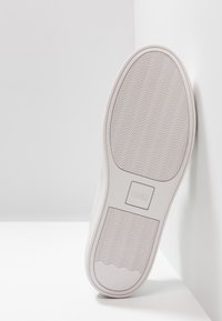 Semelle de sneaker blanche avec un motif texturé et un logo HUGO. Forme arrondie et bords lisses, présentant des rainures en forme de vague pour une meilleure adhérence.